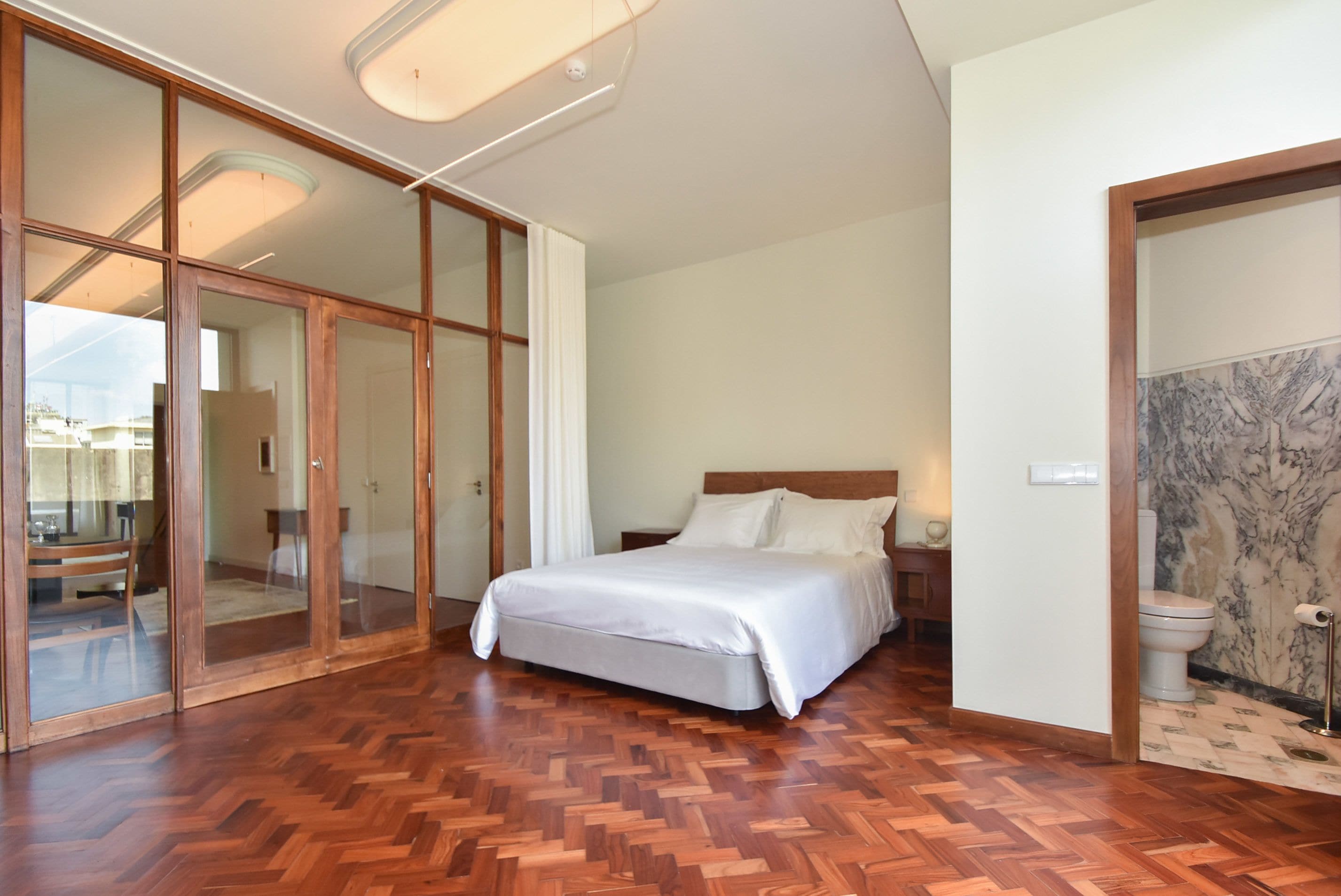 Une chambre dotée d’un grand lit, d’un plancher en bois, d’une porte vitrée donnant sur un balcon et d’un mur en marbre.