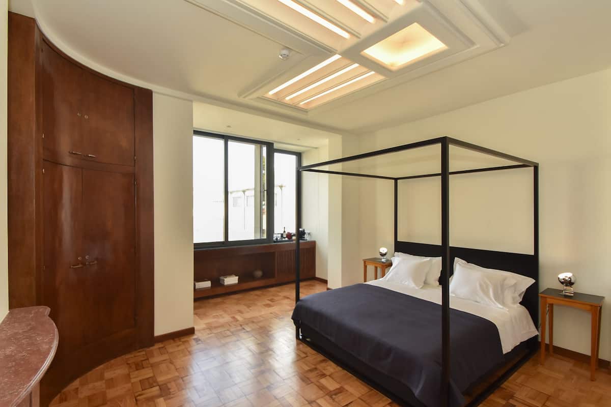 Un dormitorio con una cama con dosel, suelo de madera, un ventanal grande y un armario.