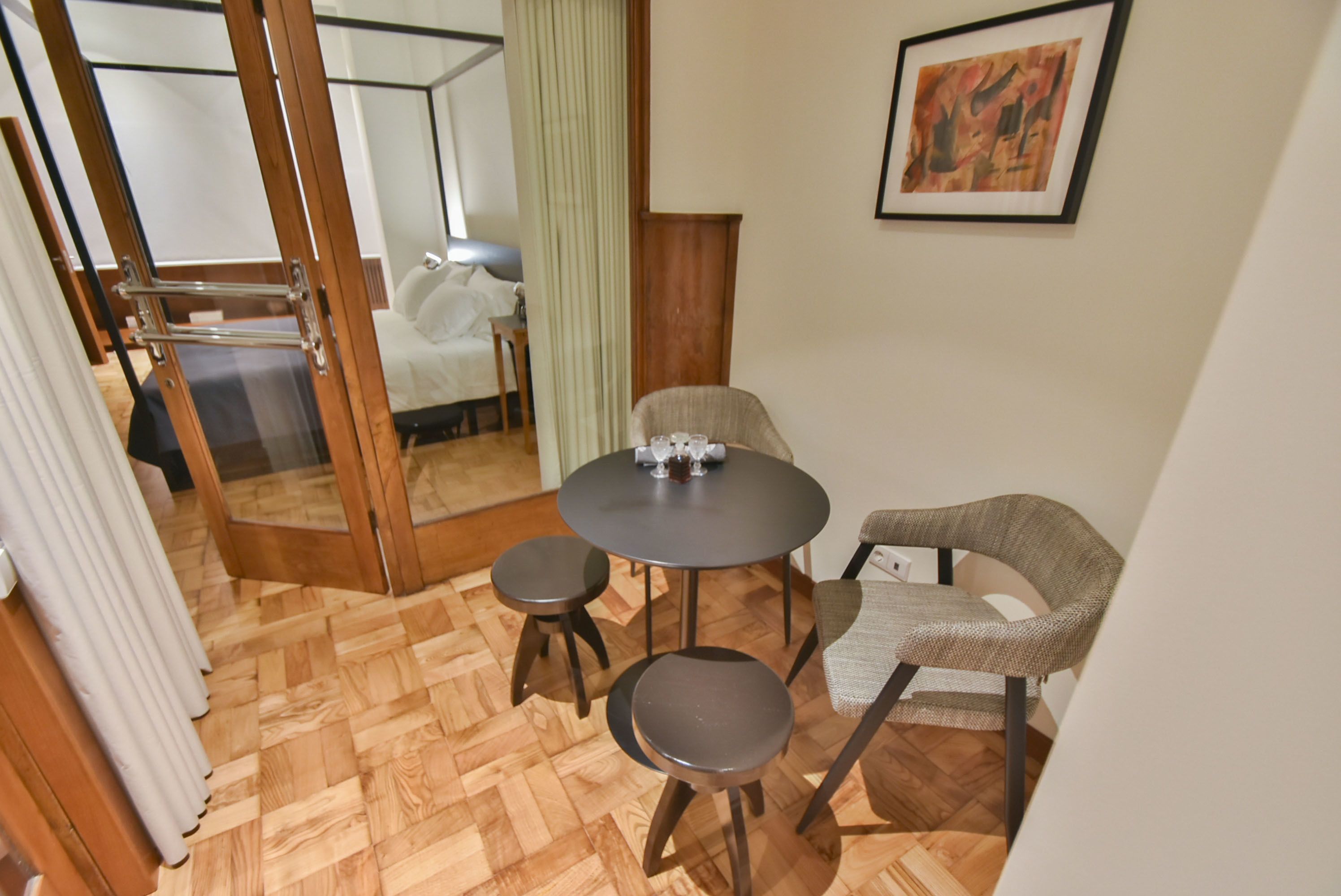 A compact room with a round table, two stools, a chair, and a bed.