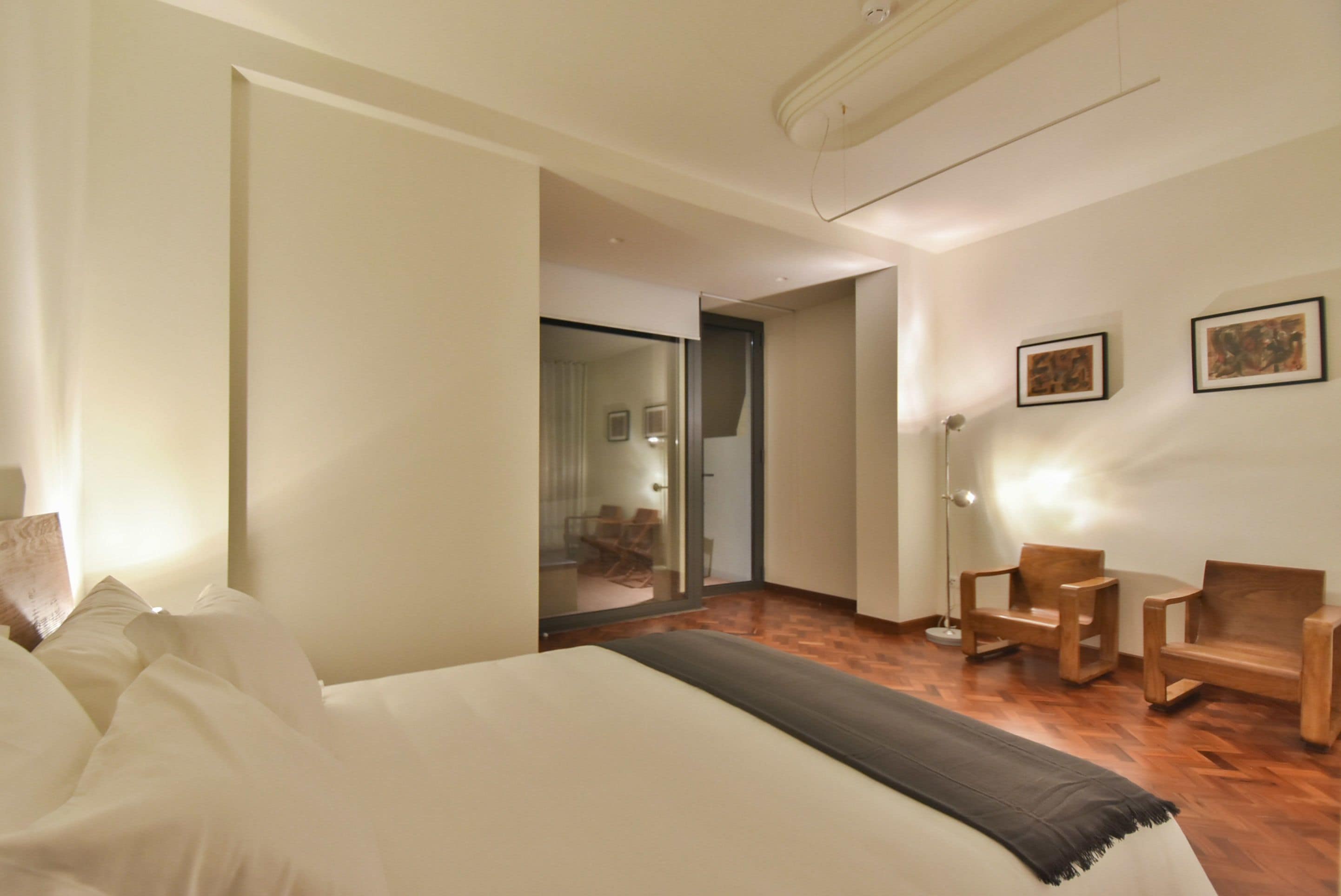 A hotel room with a bed, a wooden floor, a desk, and two chairs.