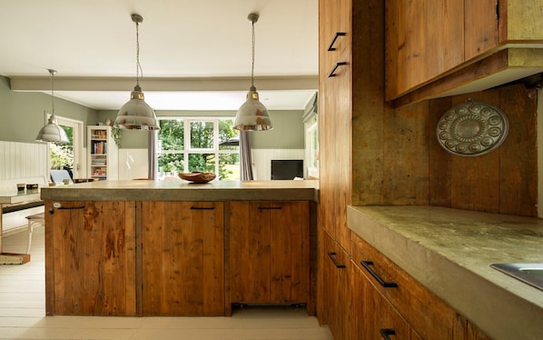 A kitchen with wooden cabinets, a central island, pendant lights, and a view of greenery outside.