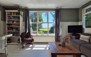A living room with a large window, a bookshelf, a sofa, a television, and a wooden table.