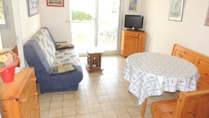 A living room with a sofa, a table, a TV, and a wooden cabinet. - Royan: T2 apartment near beach with parking (Royan)