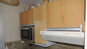 A compact kitchen with wooden cabinets, a built-in microwave, a coffee maker, and a sink. - Royan: T2 apartment near beach with parking (Royan)