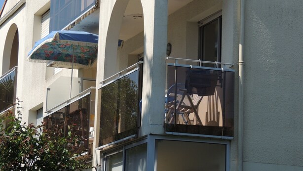 A multi-story building with balconies, large windows, and a blue umbrella. - Royan: T2 apartment near beach with parking (Royan)
