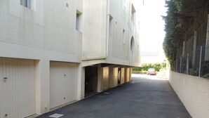 A narrow street with a building on one side and a fence on the other. There are no visible windows or doors. - Royan: T2 apartment near beach with parking (Royan)
