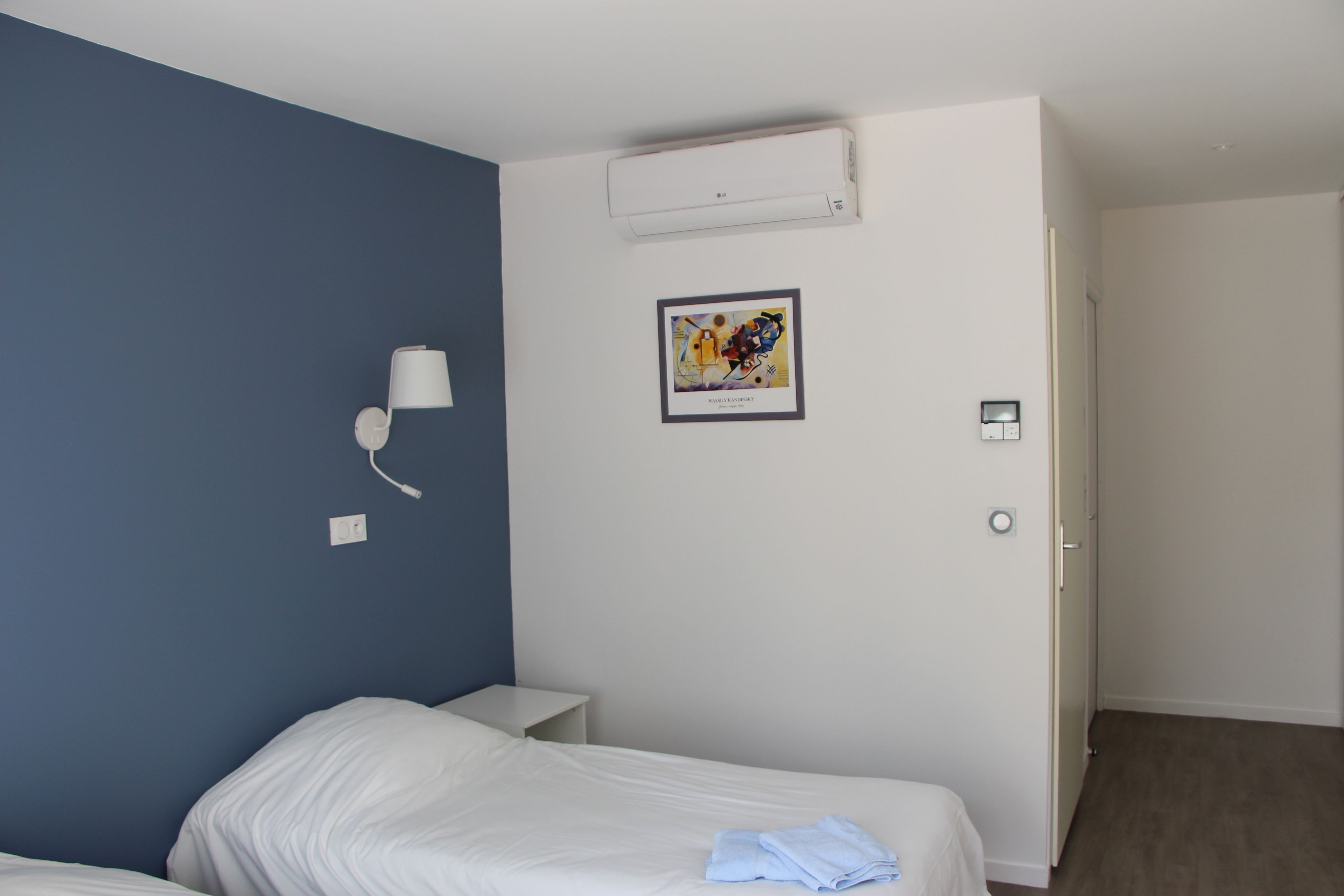 Hotelkamer met een eenpersoonsbed, nachtkastje, een wandlamp, airconditioning en een lijst aan de muur.