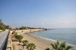 Blick auf die Küste mit Sandstrand, einer Promenade und blauem Himmel.
