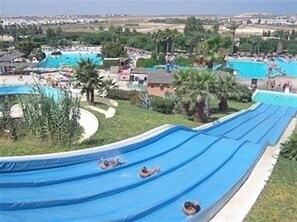 Eine Rutsche mit mehreren Bahnen, umgeben von Grünflächen und einem Poolbereich.