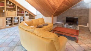 A cozy living room with a wooden ceiling, a yellow sofa, a TV, and a bookshelf.
