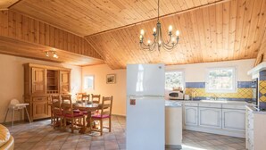 A cozy kitchen with wooden cabinets, a dining table with chairs, a refrigerator, and a window with a view.