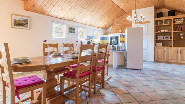 A cozy kitchen with wooden ceiling and walls, a dining table with chairs, and a refrigerator.