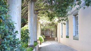 A covered walkway with columns, a stone archway, and a building with blue shutters.