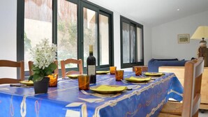 A dining area with a table set for four, large windows, and a sofa in the background.