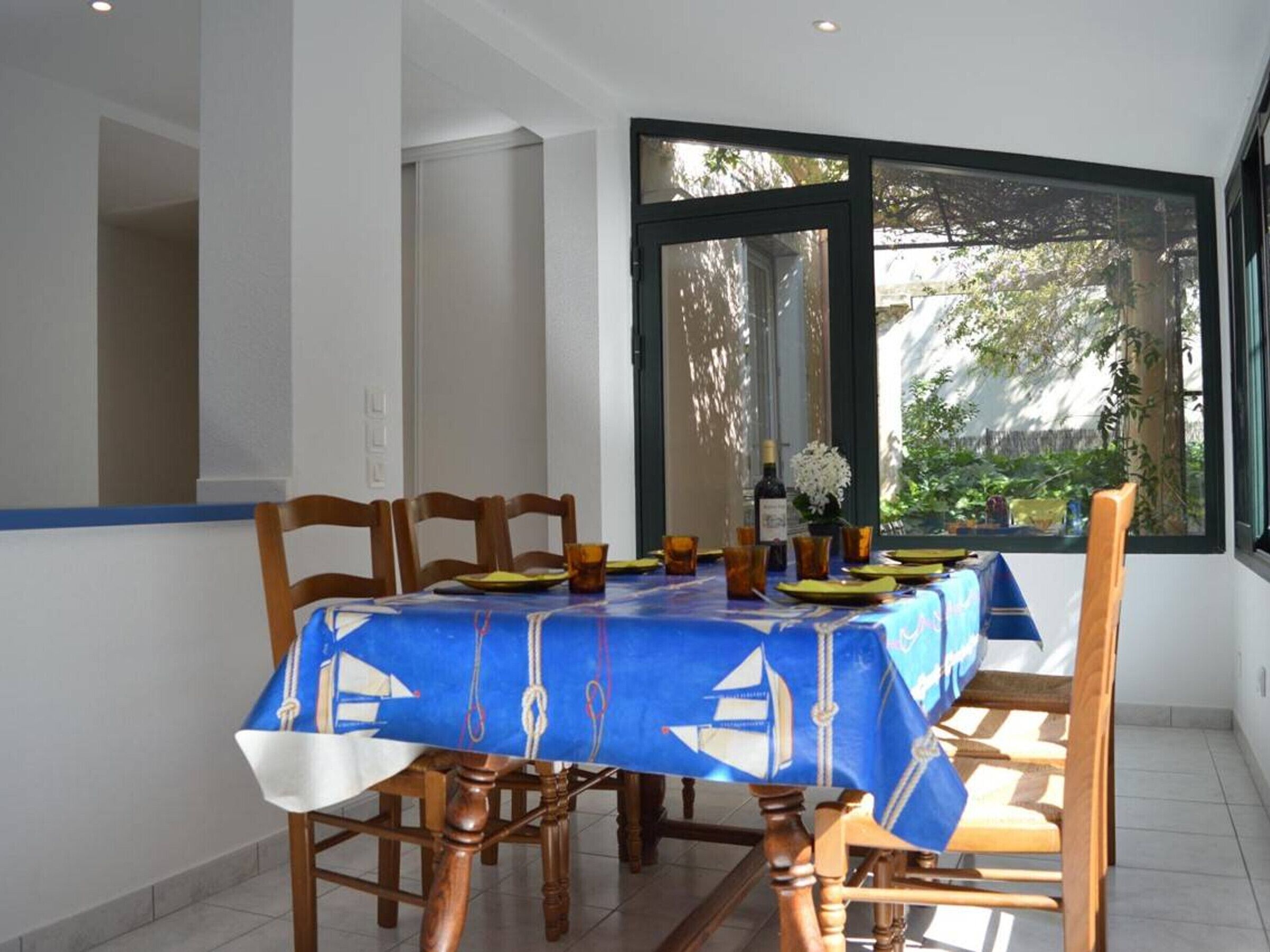 Une table à manger recouverte d’une nappe bleue, avec des chaises en bois et une bouteille de vin posée sur la table.