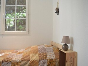A bedroom with a wooden bed, a quilt, a bedside lamp, a window with a view of trees, and a wall-mounted decoration.