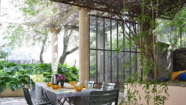 An outdoor patio with a table set for dining, surrounded by chairs and a pergola.