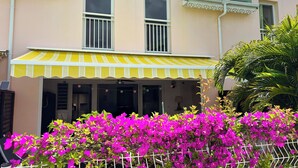 A two-story building with a yellow and white striped awning, a balcony, and a fence with pink bougainvillea flowers. - T4 Duplex of 106 m² ideally located in the center of St Francois (Saint-François)