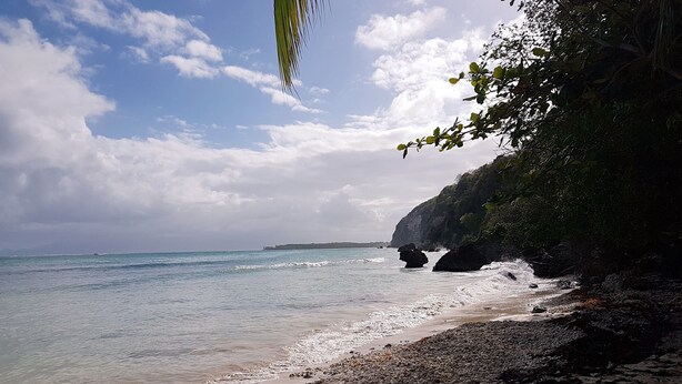 A beach with clear water, rocky shore, and a cliff with vegetation. - T4 Duplex of 106 m² ideally located in the center of St Francois (Saint-François)