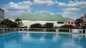 A swimming pool with a white fence, surrounded by buildings with green roofs and palm trees. - T4 Duplex of 106 m² ideally located in the center of St Francois (Saint-François)