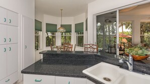 A kitchen with a granite countertop, white cabinets, and a large window overlooking a dining area. - Pet Friendly Coastal Retreat | Canal Access | Beach Nearby (New Smyrna Beach)