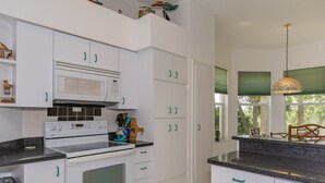A modern kitchen with white cabinets, a microwave, stove, and a dining area with a view of trees. - Pet Friendly Coastal Retreat | Canal Access | Beach Nearby (New Smyrna Beach)
