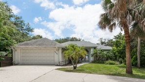 A two-story house with a garage, a small front yard, and a palm tree. - Pet Friendly Coastal Retreat | Canal Access | Beach Nearby (New Smyrna Beach)