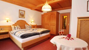 Ein schlicht eingerichtetes Schlafzimmer mit Holzbett, Nachttischlampen, einem Holzschrank und einem Tisch mit einem Glas Champagner und Rosenblättern.