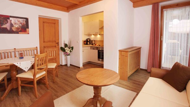 Ein gemütliches Wohnzimmer mit einem Holzesstisch, Stühlen, einer Couch und einer Küche im Hintergrund.