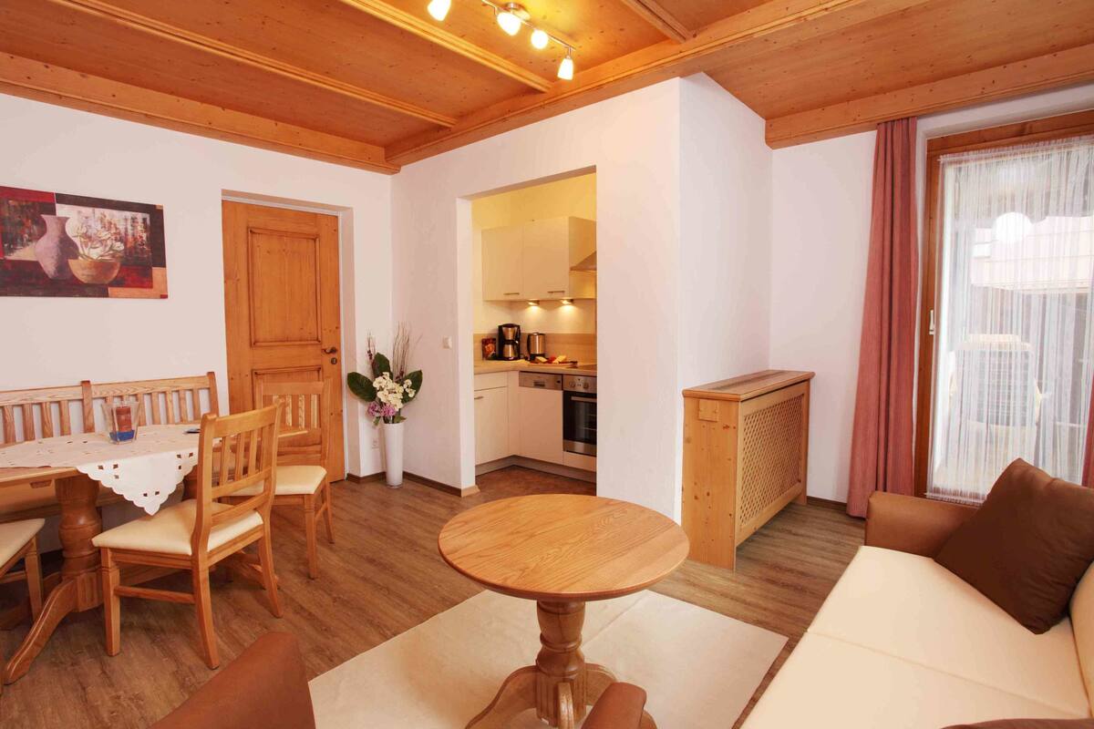 Un salon chaleureux avec une table à manger en bois, des chaises, un canapé et une cuisine en arrière-plan.