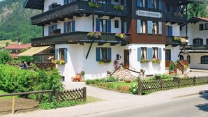 Ein zweistöckiges Gebäude mit einem Schild, auf dem "Grim Rottmeister" steht. Es verfügt über Balkone mit Blumenkästen, eine Steintreppe und einen Holzzaun davor.