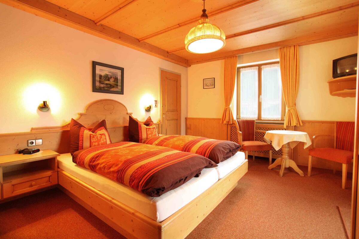 Une chambre d’hôtel confortable avec un lit en bois, des lampes de chevet, une petite table et une chaise.