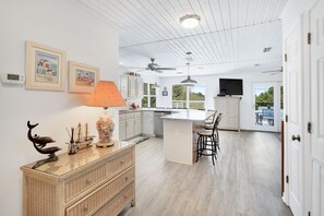 A modern kitchen with white cabinetry, a central island, and a dining area with bar stools. - Hms Sunrise & Sunset | Gulf Views, Private Pool, Dedicated Beach Access (Santa Rosa Beach)
