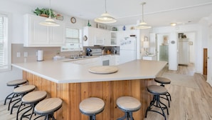 Una cocina moderna con una isla grande, taburetes de bar, armarios blancos e iluminación colgante.