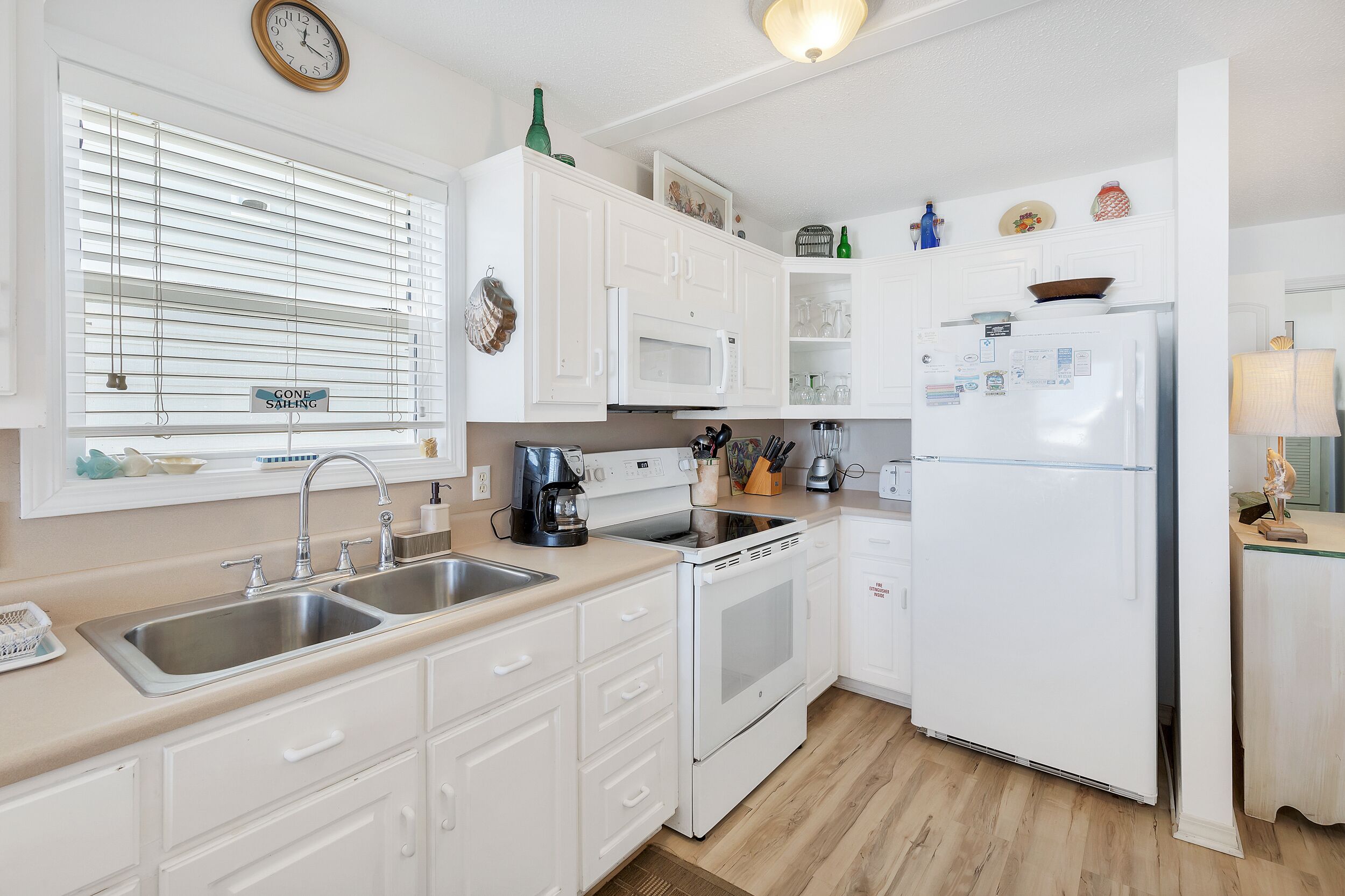 A kitchen with white cabinets, a double sink, a microwave, an oven, and a refrigerator.