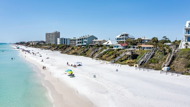 Una playa de arena blanca, agua turquesa cristalina y una hilera de edificios con balcones con vista a la playa.