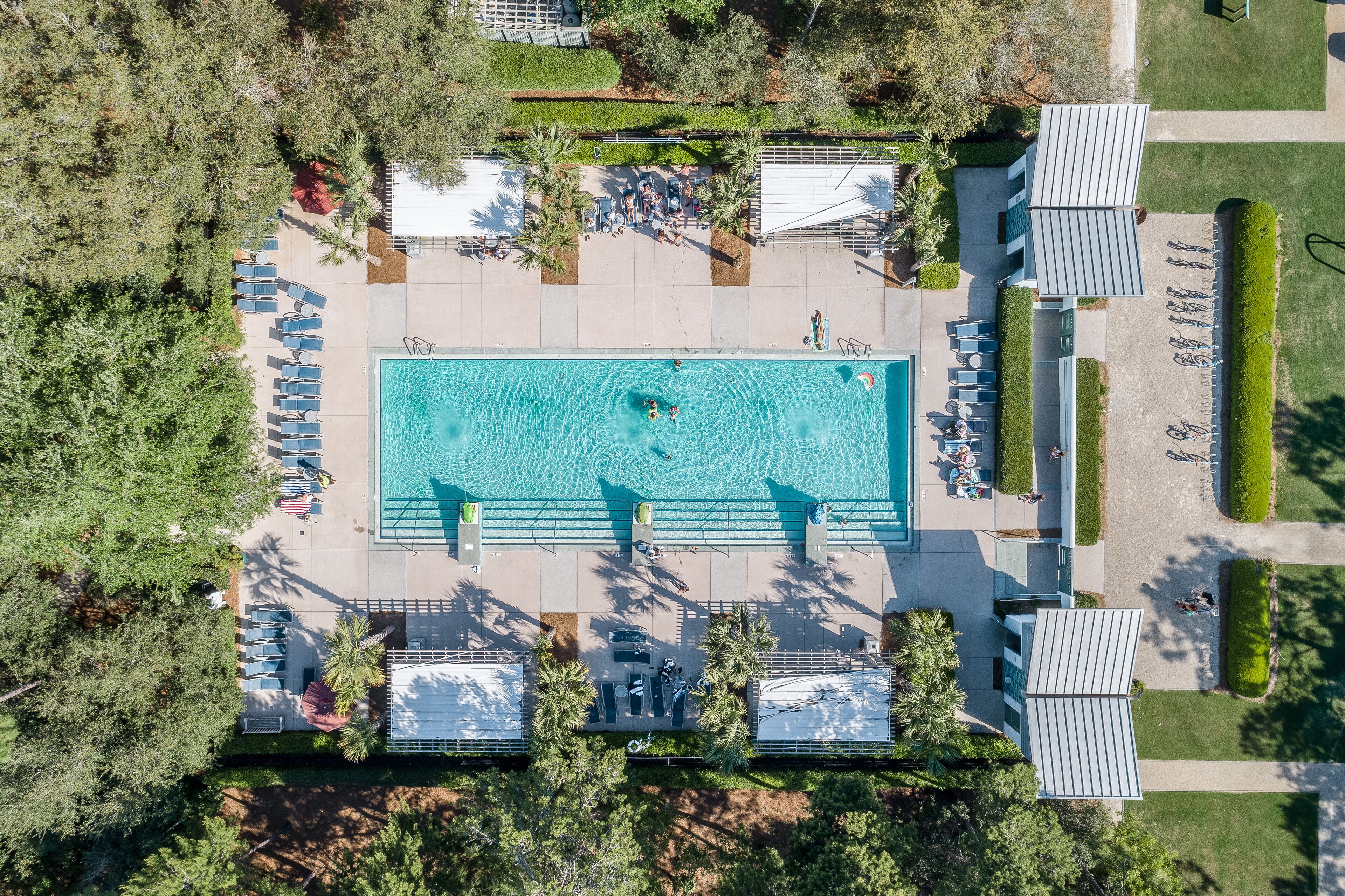 An aerial view of a swimming pool area with lounge chairs, a pool, and surrounding greenery.