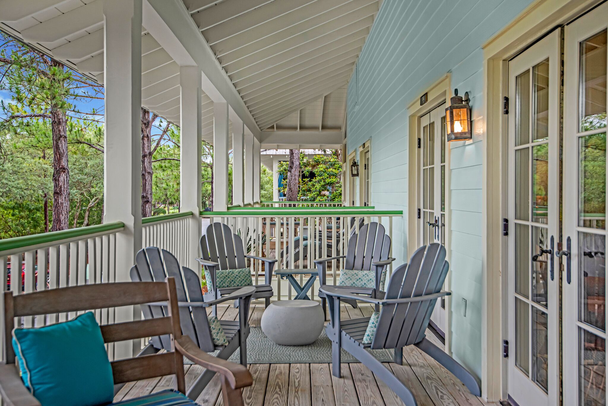 Eine überdachte Veranda mit Adirondack-Stühlen und einer Bank, einem kleinen Tisch und einem Laternen.
