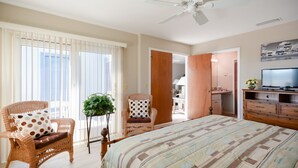 Ein Schlafzimmer mit einem Bett, zwei Korbstühlen, einem Deckenventilator und einem Fernseher.