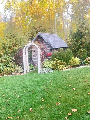 Un chalet rustique en rondins de bois, doté d’une entrée en forme d’arche, entouré d’une pelouse bien entretenue et d’un feuillage automnal.