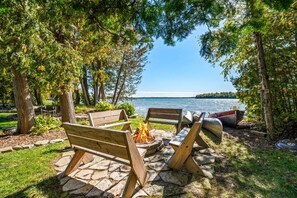 An outdoor seating area with a fire pit, benches, and a view of a lake.