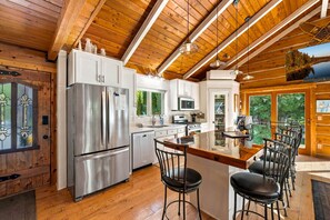 A modern kitchen with stainless steel appliances, a central island with bar stools, and a view of the outdoors through large windows.