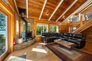 A log cabin interior with a stone fireplace, leather sofa, and a view of the outdoors.