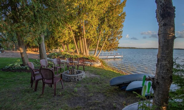 A lakeside seating area with chairs and a fire pit, surrounded by trees and overlooking the water.