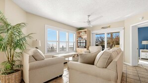 Ein Wohnzimmer mit zwei Sofas, einem Couchtisch, einem Deckenventilator und einem großen Fenster mit Jalousien.