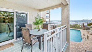 Ein Balkon mit Glastür, Tisch und Stühlen, ein kleiner Pool und Blick auf das Meer und eine Brücke.