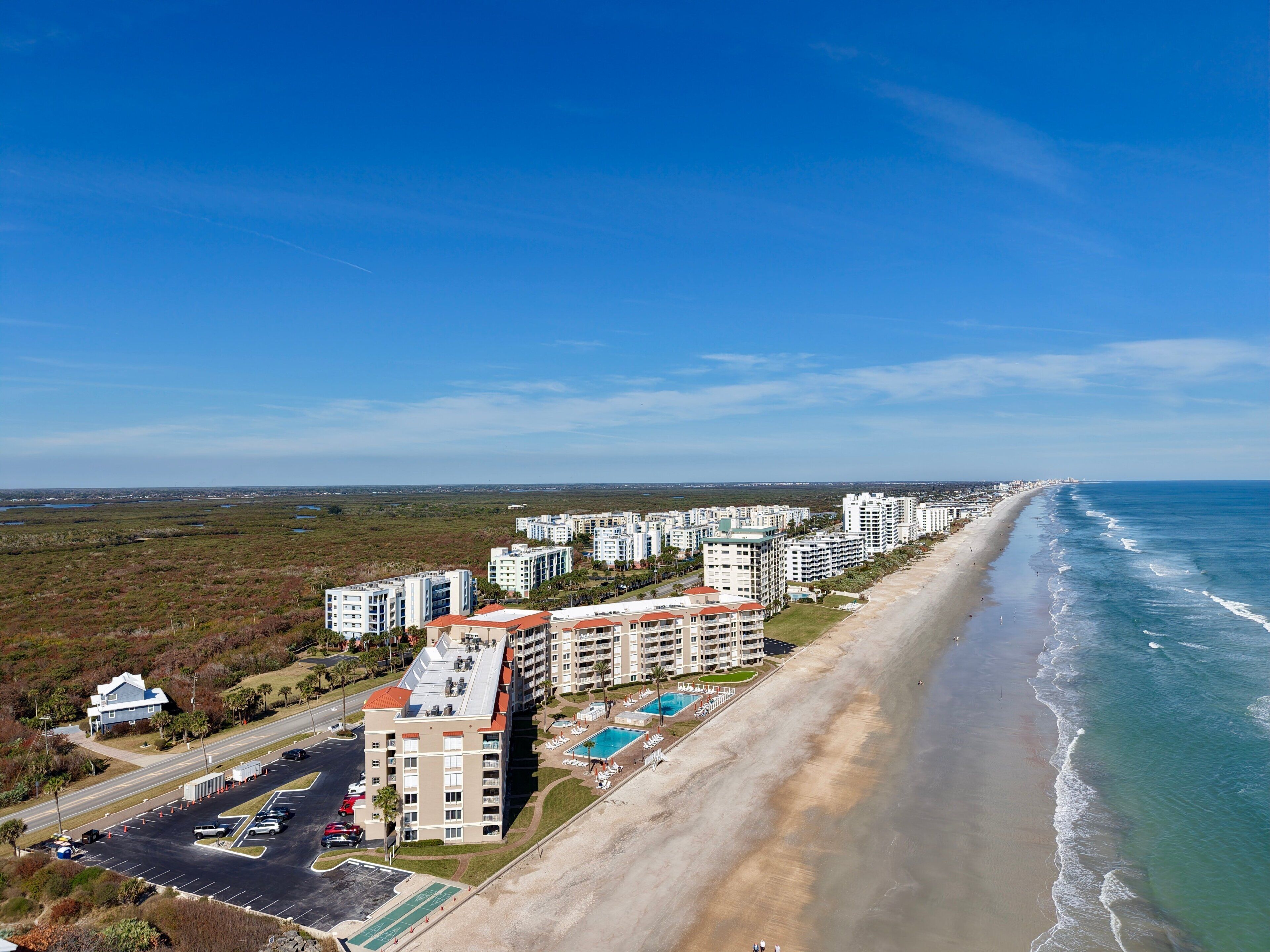 Ett hotell vid kusten med flera byggnader, en strand och en parkeringsplats.