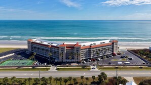 A hotel with a curved roof, multiple floors, and a parking lot with several cars.