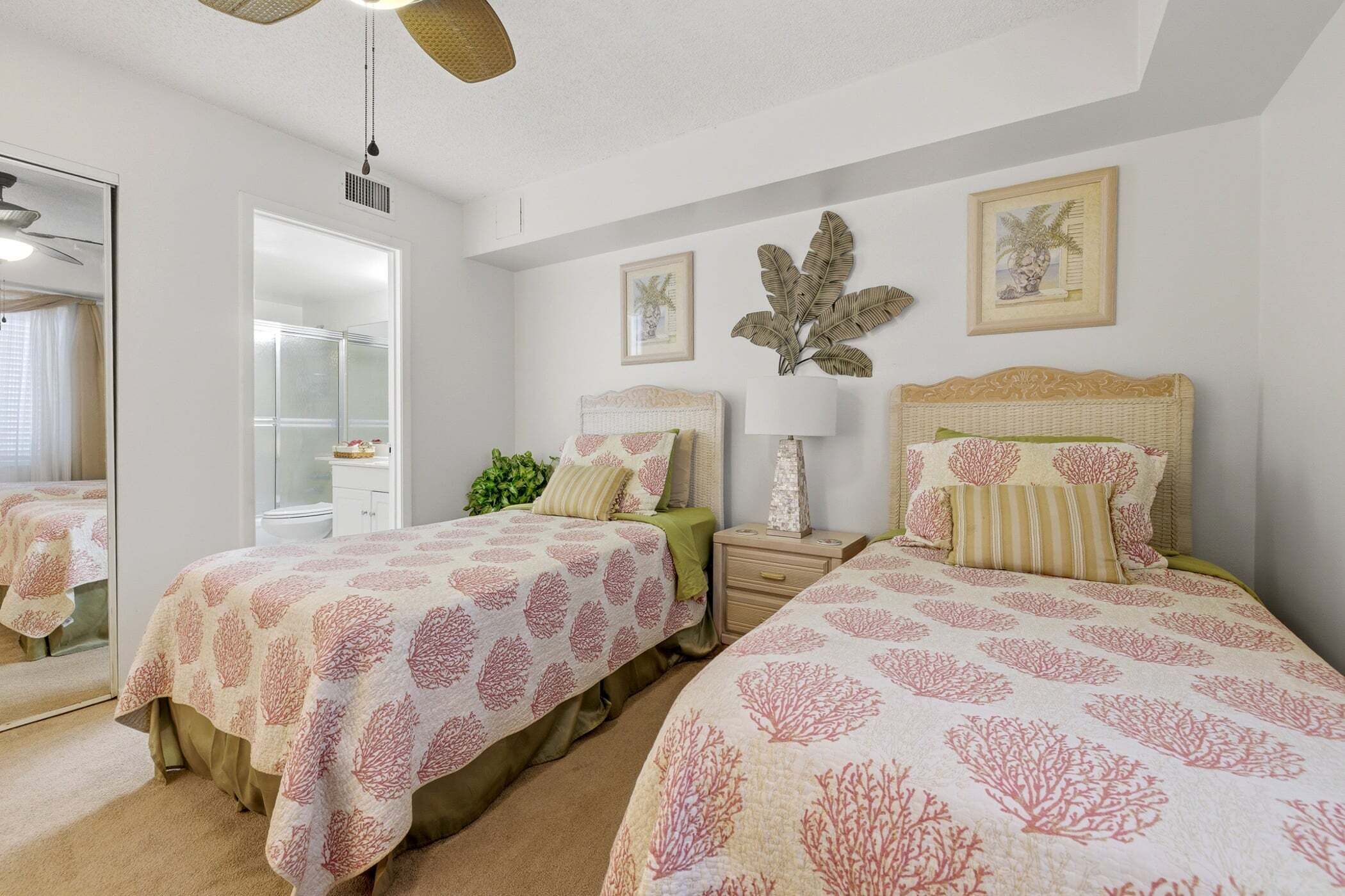 A bedroom with two beds, a nightstand, a mirror, and a ceiling fan.