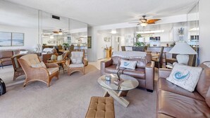 A spacious living room with a large mirror, comfortable seating, and a ceiling fan.